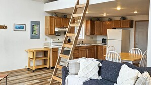 Un espacio habitable compacto con cocina, comedor y un dormitorio en entrepiso al que se accede por una escalera de madera.