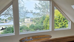 Una habitación con techo inclinado y un ventanal grande que da a una calle con árboles y un edificio que dice "DOLLAR GENERAL".