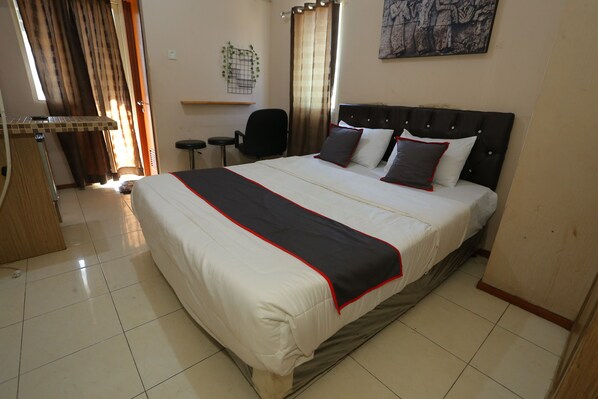 Quarto de hotel com uma cama grande, uma escrivaninha, uma cadeira e uma janela com cortinas.