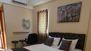 A neatly made bed with a black and red bedspread, a black upholstered headboard, and a wall-mounted air conditioner.
