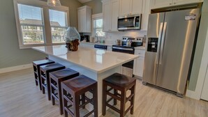 Una cocina moderna con gabinetes blancos, electrodomésticos de acero inoxidable y una isla grande con taburetes de bar.