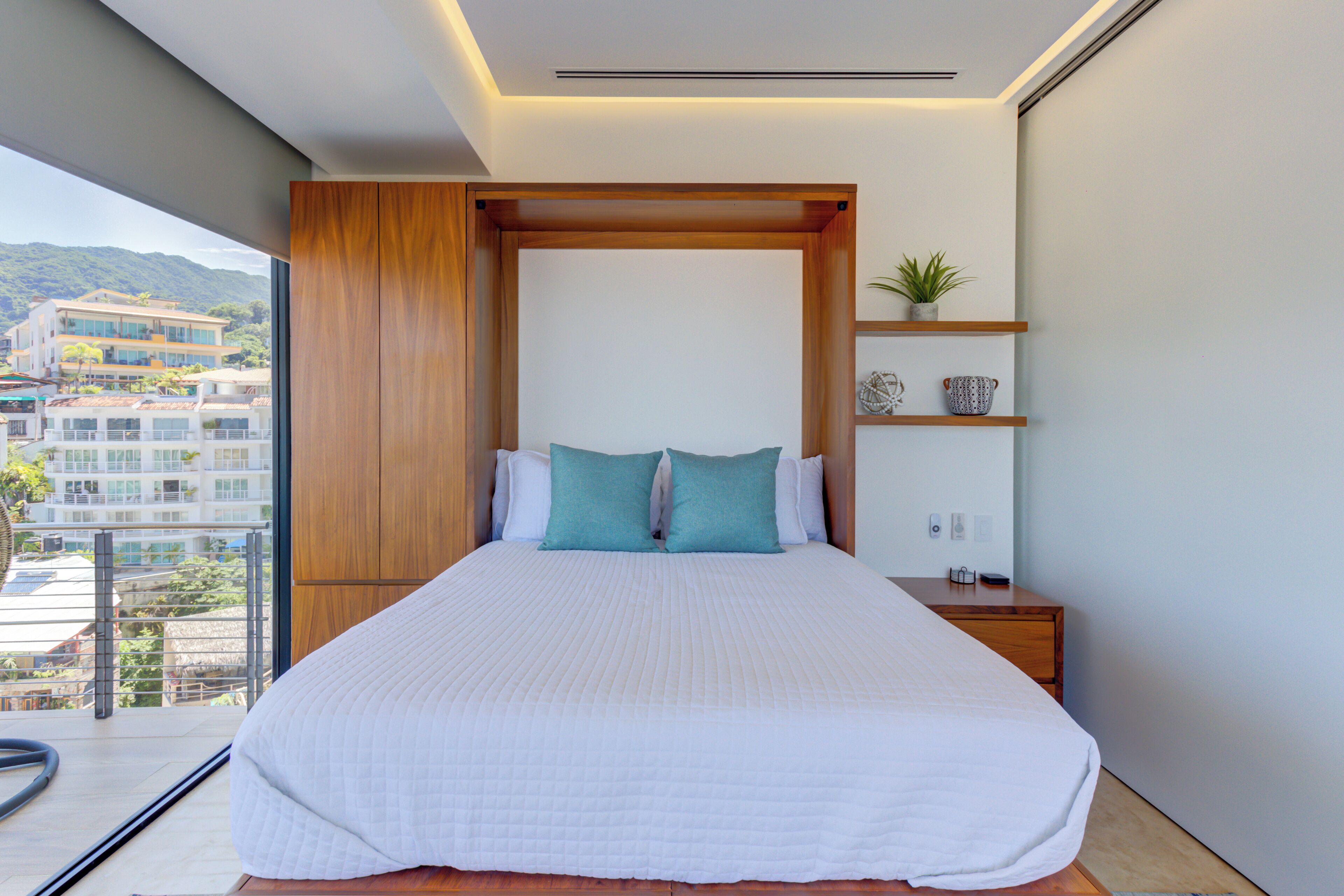 Un dormitorio moderno con una cama grande, cabecera de madera y vistas a un paisaje urbano.
