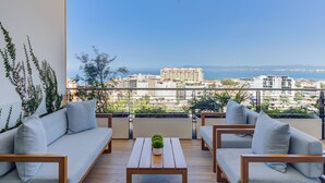 Un balcon avec une table en bois et deux canapés, donnant sur un paysage urbain avec des bâtiments et un ciel dégagé.