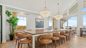 A spacious dining area with a long wooden table and leather chairs, large windows, and a view of the ocean. - Island Enchantment - Oceanfront Pet Friendly w/ Cabana Service (Kill Devil Hills)