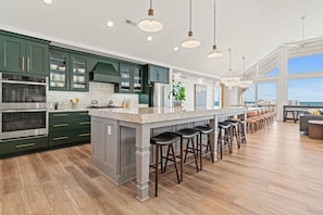 A modern kitchen with dark green cabinets, stainless steel appliances, and a large island with bar stools.