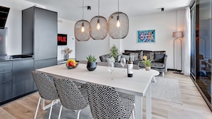 Une cuisine moderne avec un plan de travail blanc, des chaises aux motifs noirs et blancs et des suspensions en osier.