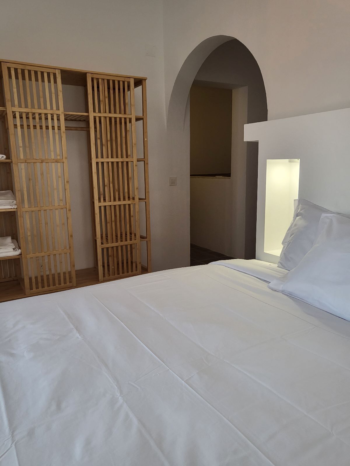 A bedroom with a bed, a wooden wardrobe, and an arched doorway.