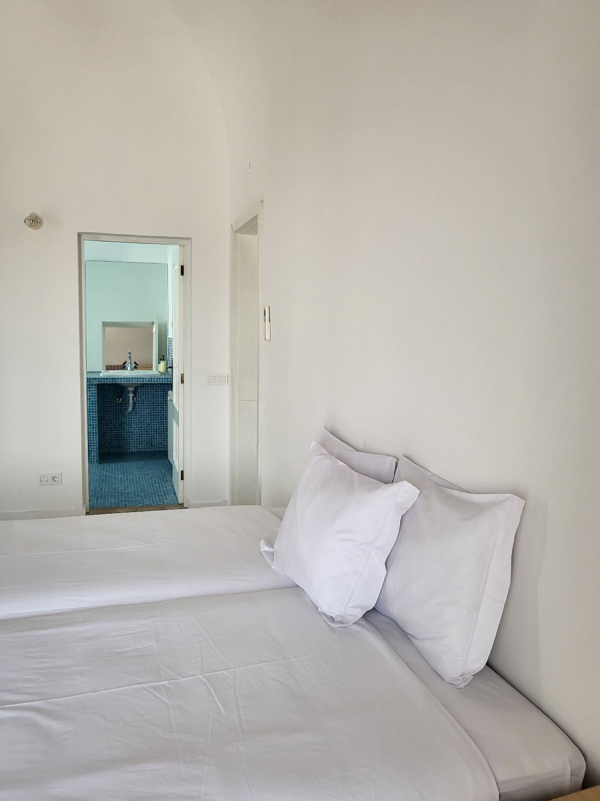 A hotel room with a bed, a white pillow, and a bathroom visible through an open door.