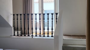 A bedroom with a bed, a window with curtains, a balcony with a railing, and a staircase. - Solar de Arraiolos (Arraiolos)