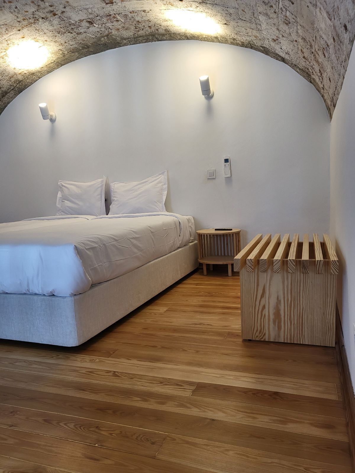 A bedroom with a bed, a small wooden side table, and a built-in bench.