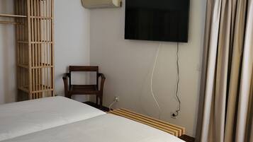 Una habitación de hotel con una cama, un televisor en la pared, una silla de madera y una ventana con cortinas.
