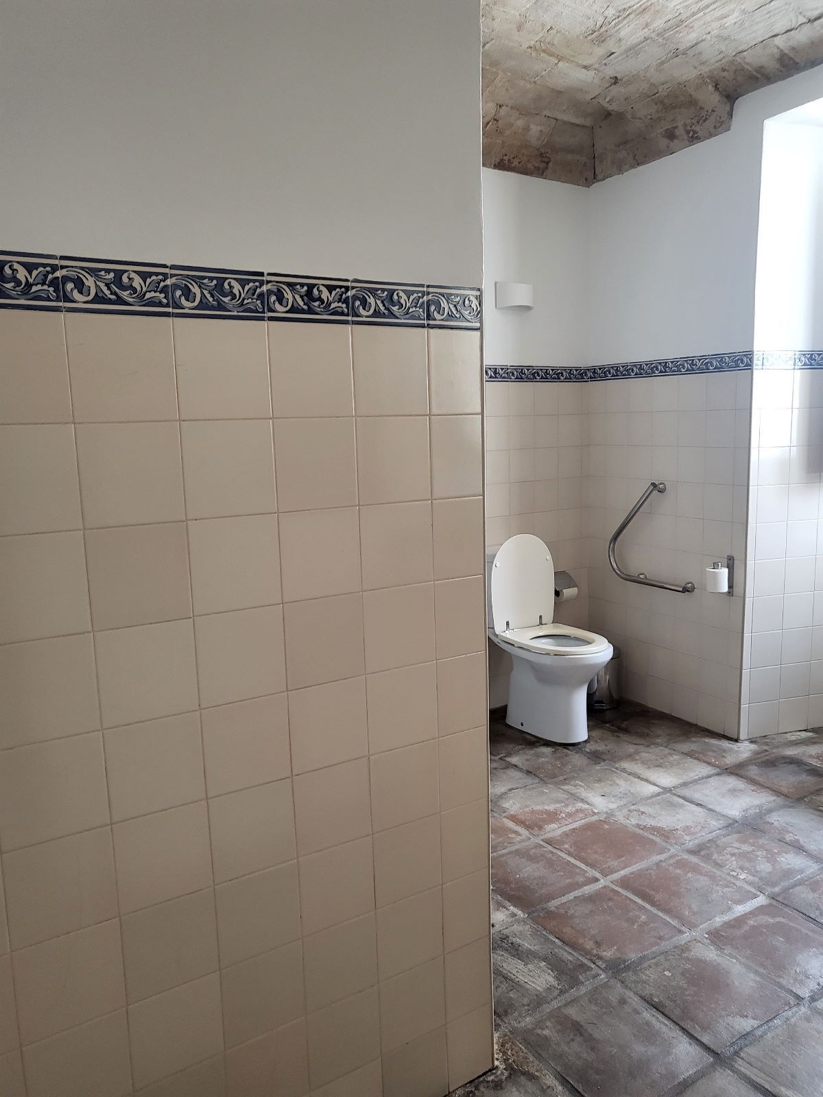 A bathroom with a toilet, a handrail, and a tiled floor.