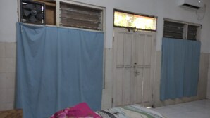 Una habitació amb un llit, una finestra amb cortina, una porta i un aire condicionat fixat a la paret.