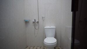 Un banyet petit amb vàter, dutxa i dispensador de paper higiènic.