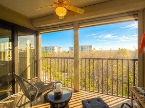 A balcony with a glass door, a ceiling fan, and a view of buildings and trees.