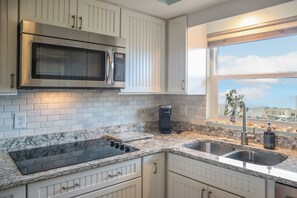 Une cuisine avec des meubles blancs, un four à micro-ondes encastré, une cuisinière à gaz, une machine à café et une fenêtre donnant sur un beau paysage.