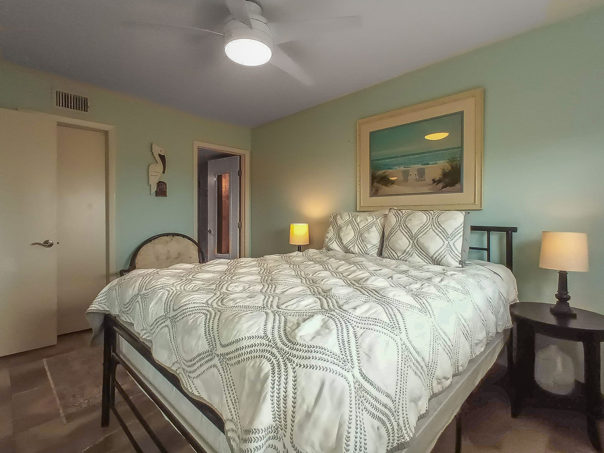 Une chambre à coucher avec un lit, deux lampes de chevet, une porte, une chaise et un tableau au mur.