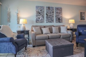 A living room with a sofa, two armchairs, a coffee table, and a patterned rug. There are three wall-mounted lamps and a decorative wall piece.