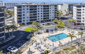Un edificio residencial de varios pisos con piscina en la azotea, rodeado de palmeras y mobiliario de exterior.