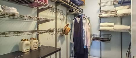 A laundry room with shelves holding towels, bottles, and a drying rack.