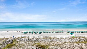 Une plage avec une promenade en bois menant au rivage, une eau d’un bleu limpide et des parasols verts.