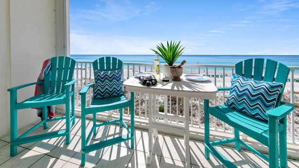 Un balcon avec des chaises turquoise et une table, donnant sur une plage.