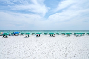 Una playa con hileras de sombrillas verdes y sillas de playa.