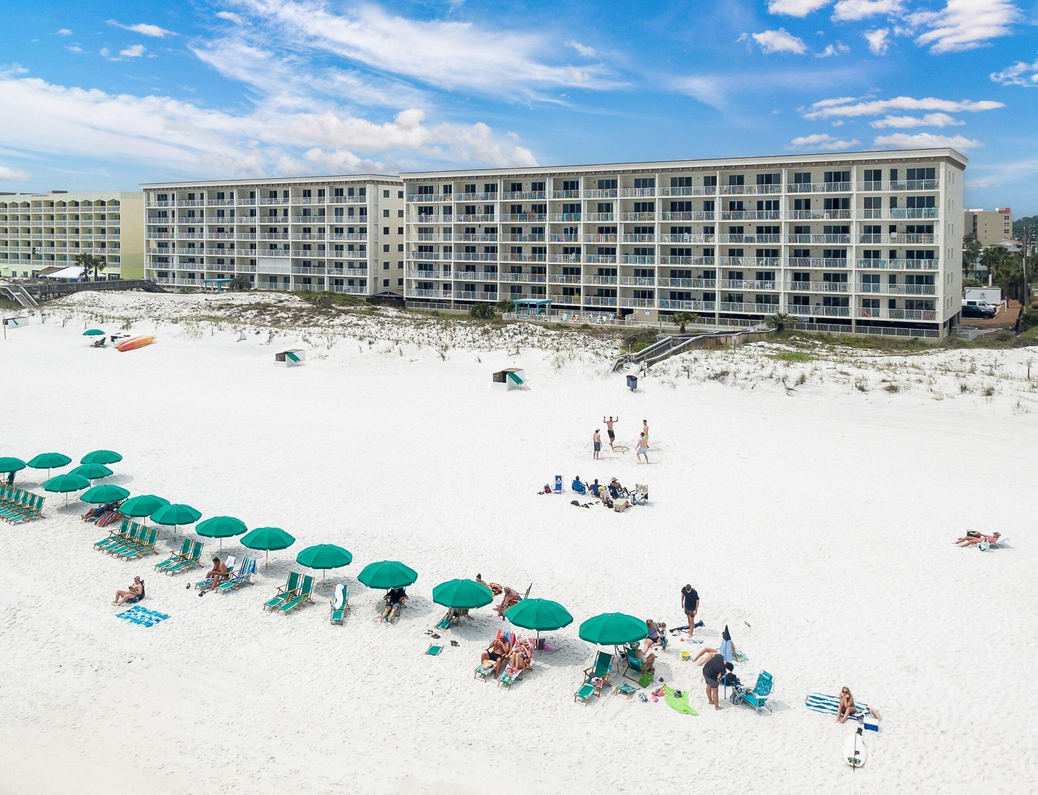 A beachfront hotel with multiple balconies, beach umbrellas, and lounge chairs.