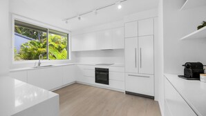 Eine moderne Küche mit weißen Schränken, einem eingebauten Backofen und einem Fenster mit Blick auf Grünflächen.