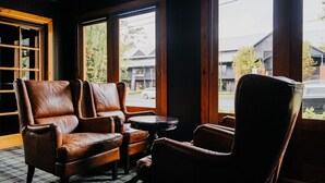 A room with two leather armchairs, a small round table, and a window with a view of a street and buildings. - The Amalfi 20 bedrooms, exclusive use (Hepburn Springs)