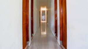 Un largo pasillo estrecho con puertas de madera a ambos lados, que conduce a una habitación luminosa al final.