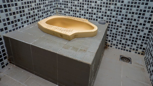 Una bañera pequeña y cuadrada con interior color beige, rodeada por un muro de azulejos con un diseño de mosaico.