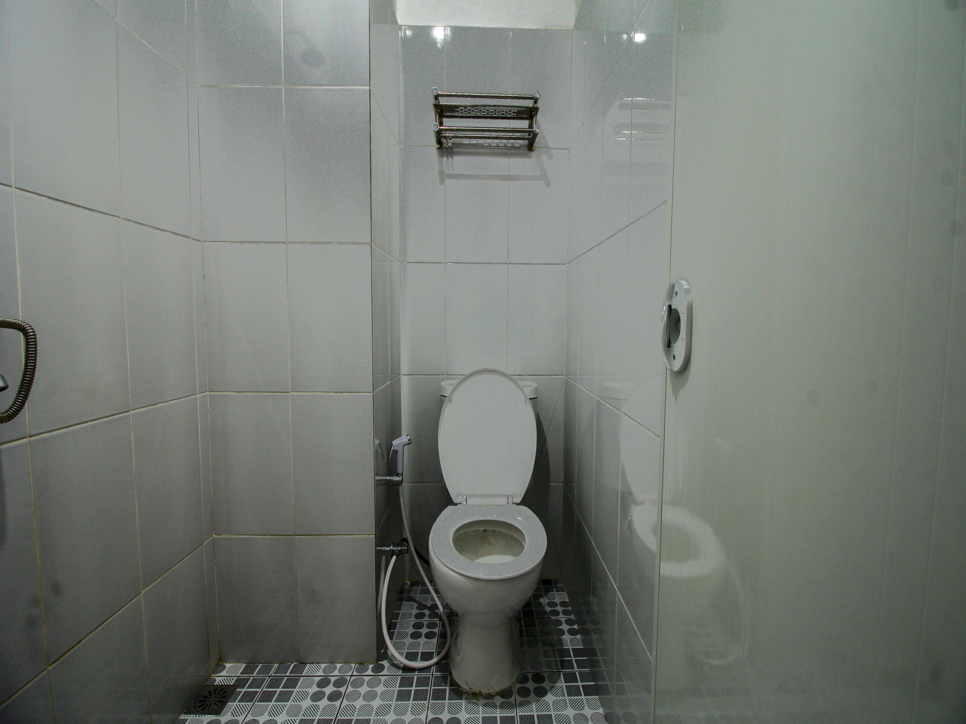 A small, tiled bathroom with a toilet, a hand dryer, and a toilet paper holder.