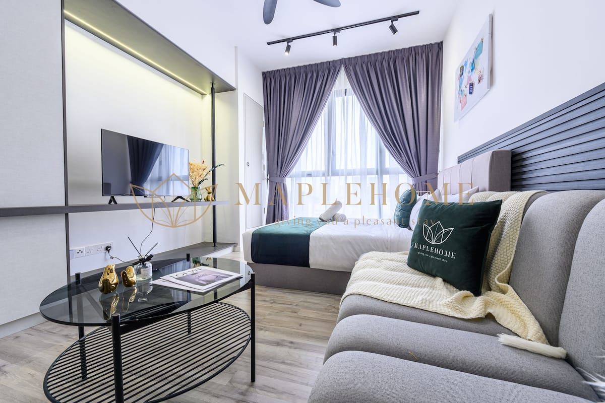 A modern hotel room with a bed, a sofa, a TV, and a glass table with decorative items.