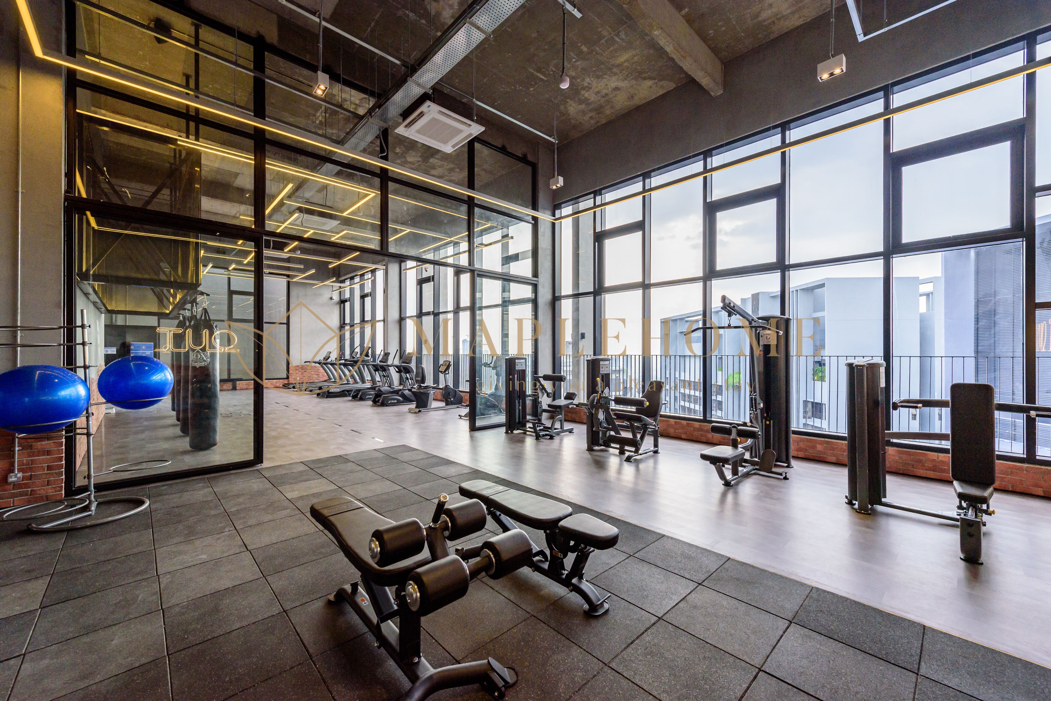 Una palestra con diverse attrezzature per esercizi, ampie finestre e un muro in mattoni.