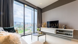 Uma sala de estar moderna com um sofá, uma mesa de centro de vidro e uma televisão de tela plana em um móvel branco.