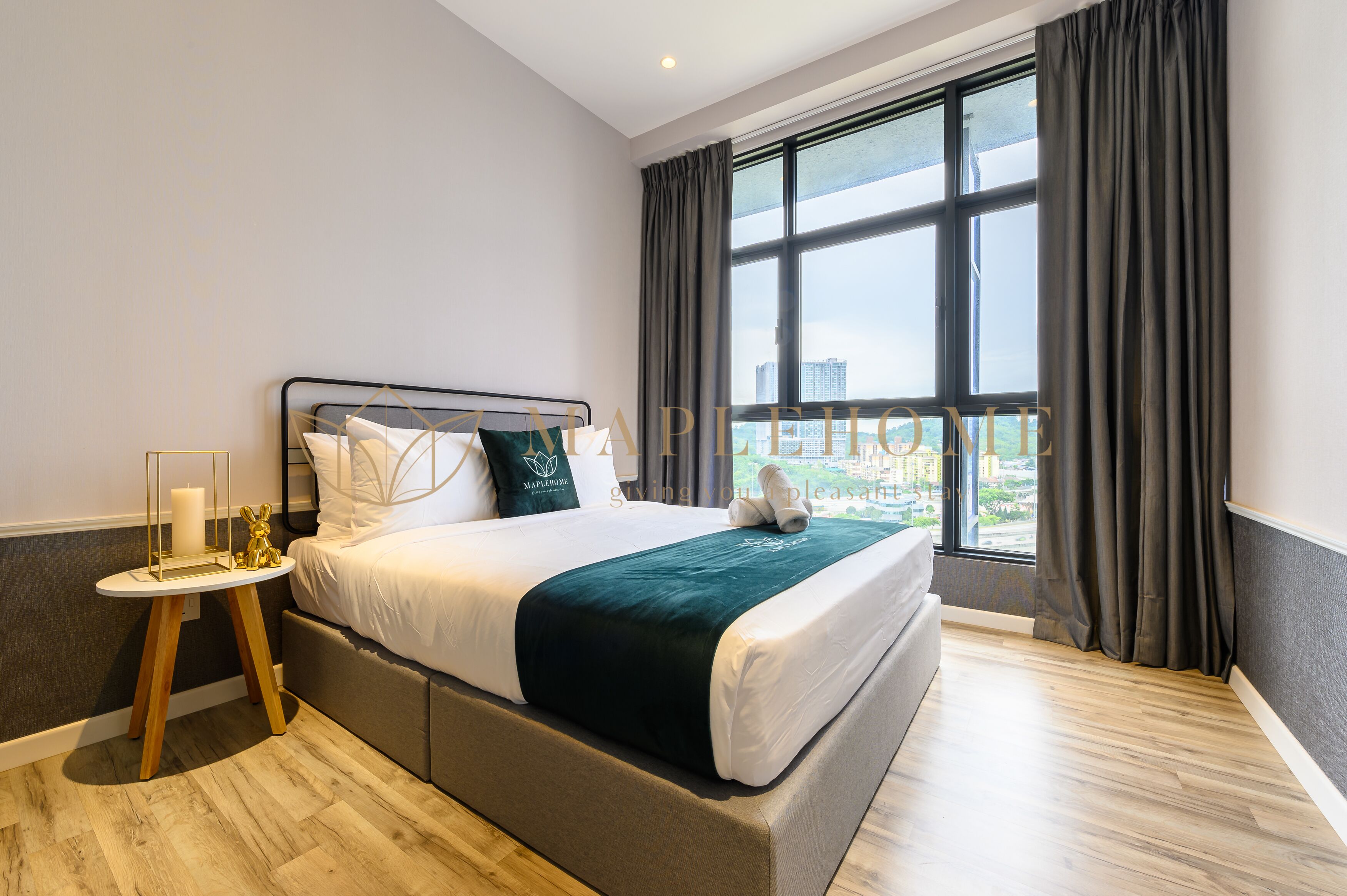 A modern hotel room with a large bed, a bedside table with a candle, and a view of the city through large windows.