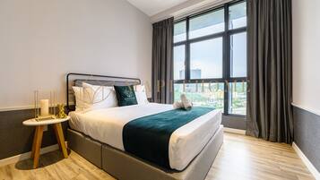 A modern hotel room with a large bed, a bedside table with a candle, and a view of the city through large windows.