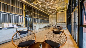 Um interior moderno com pé-direito alto, dutos aparentes e uma área de estar com cadeiras de vime e uma mesa.