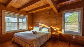 A wooden cabin bedroom with a bed, bedside lamps, and large windows.
