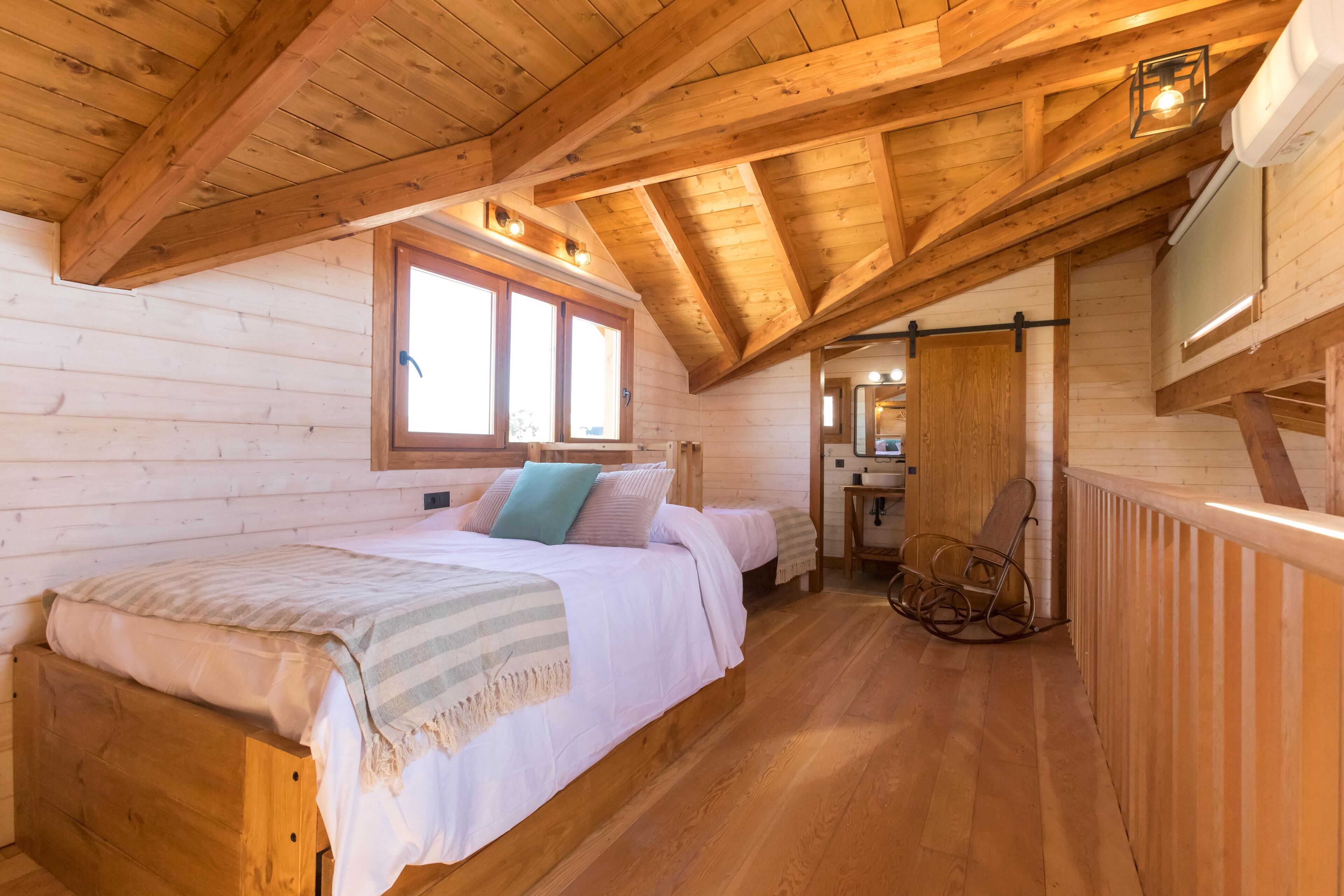 Accogliente camera da letto in una baita di legno, con un letto, cuscini, una poltrona a dondolo e una finestra.
