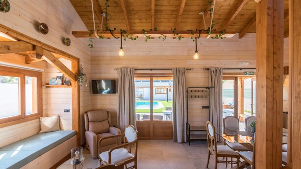 Un interno di una baita in legno con un'area salotto, un tavolo da pranzo e una TV montata a parete.