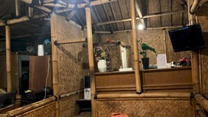 A bamboo-framed room with a bed, a television, and a small table with a plant and decorative items. - OYO 93159 Resort Cinta Kasih (Megamendung)