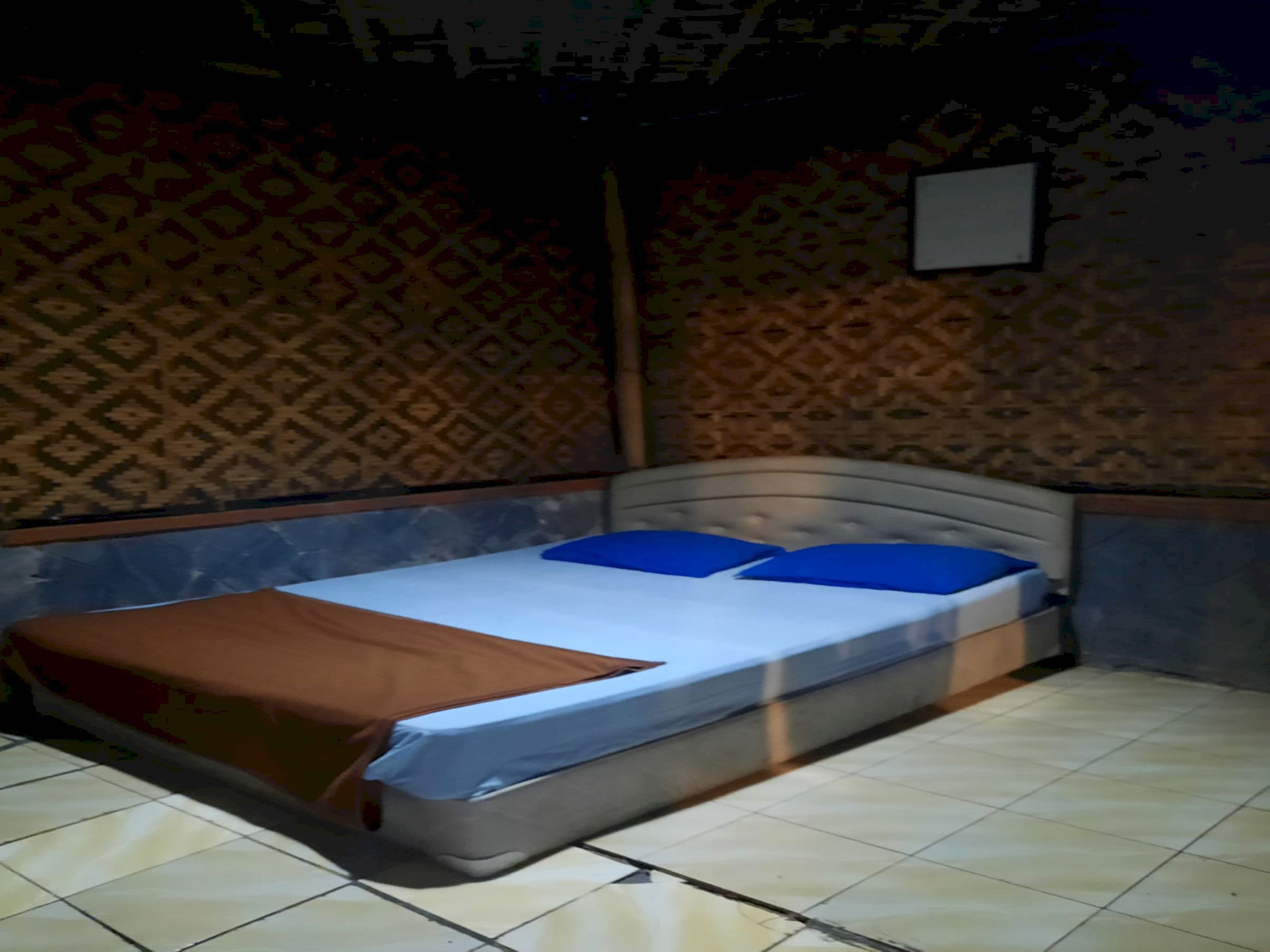 A bedroom with a bed, patterned wallpaper, and a tiled floor.