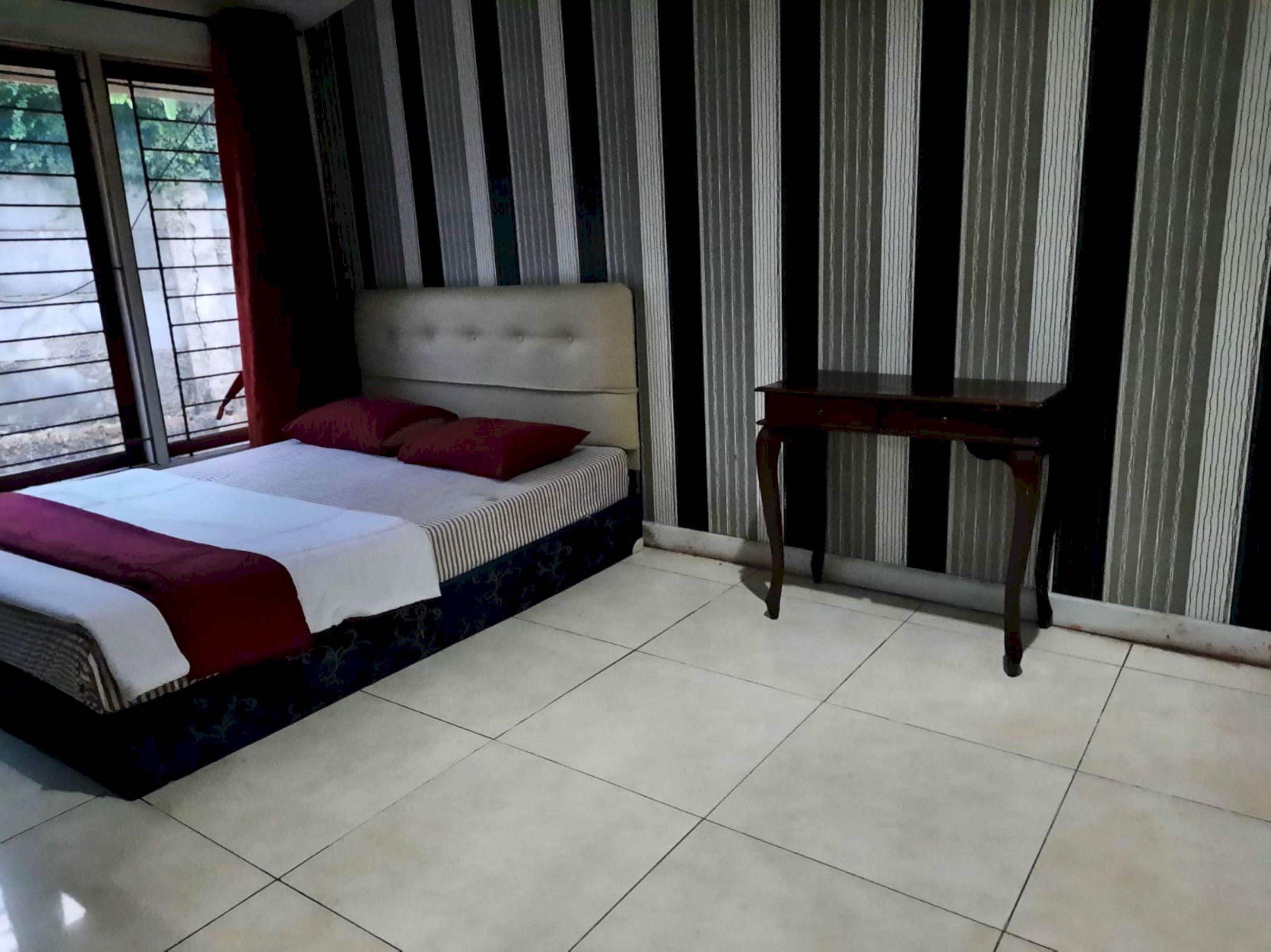 A bedroom with a bed, a nightstand, and a window with curtains.