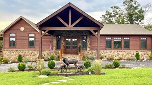 A two-story log cabin with a stone foundation, a covered porch, and a deer sculpture in the front yard. - The Dogwood Inn (Blue Ridge)