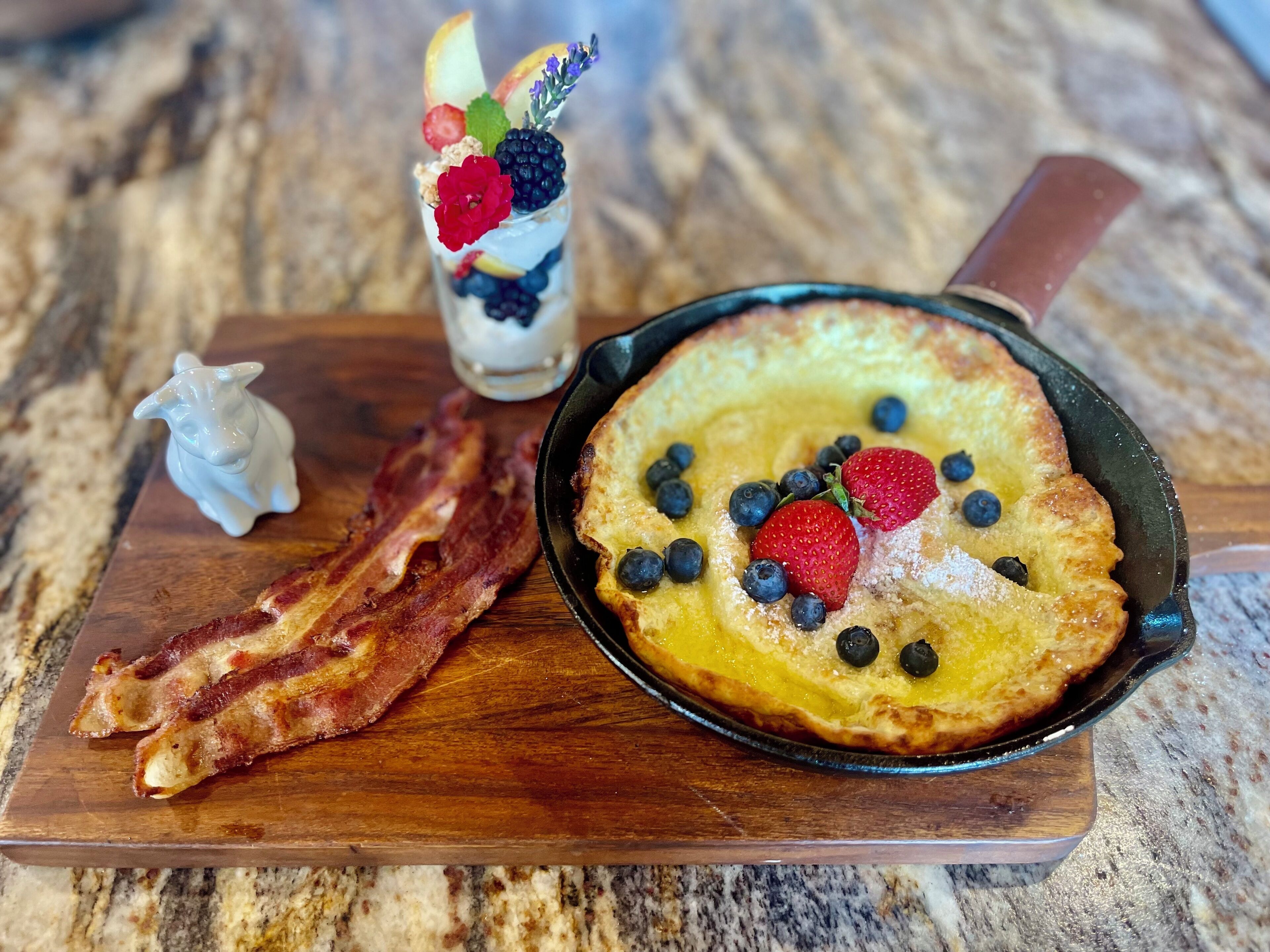 Prato de café da manhã com panquecas, bacon e uma bebida com frutas.