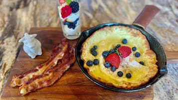 Prato de café da manhã com panquecas, bacon e uma bebida com frutas.