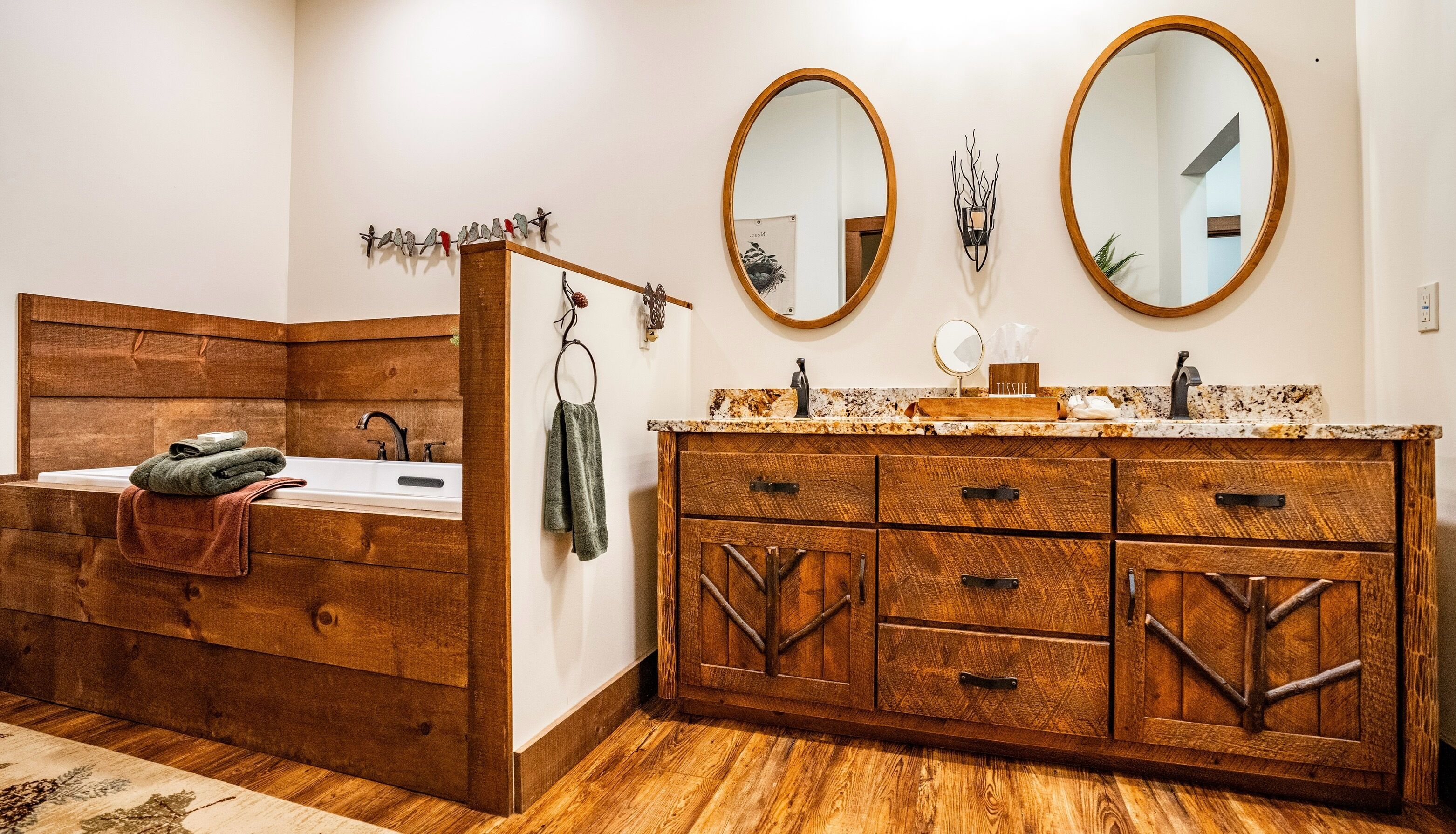 A bathroom with a wooden vanity, two round mirrors, a sink, and a towel rack.
