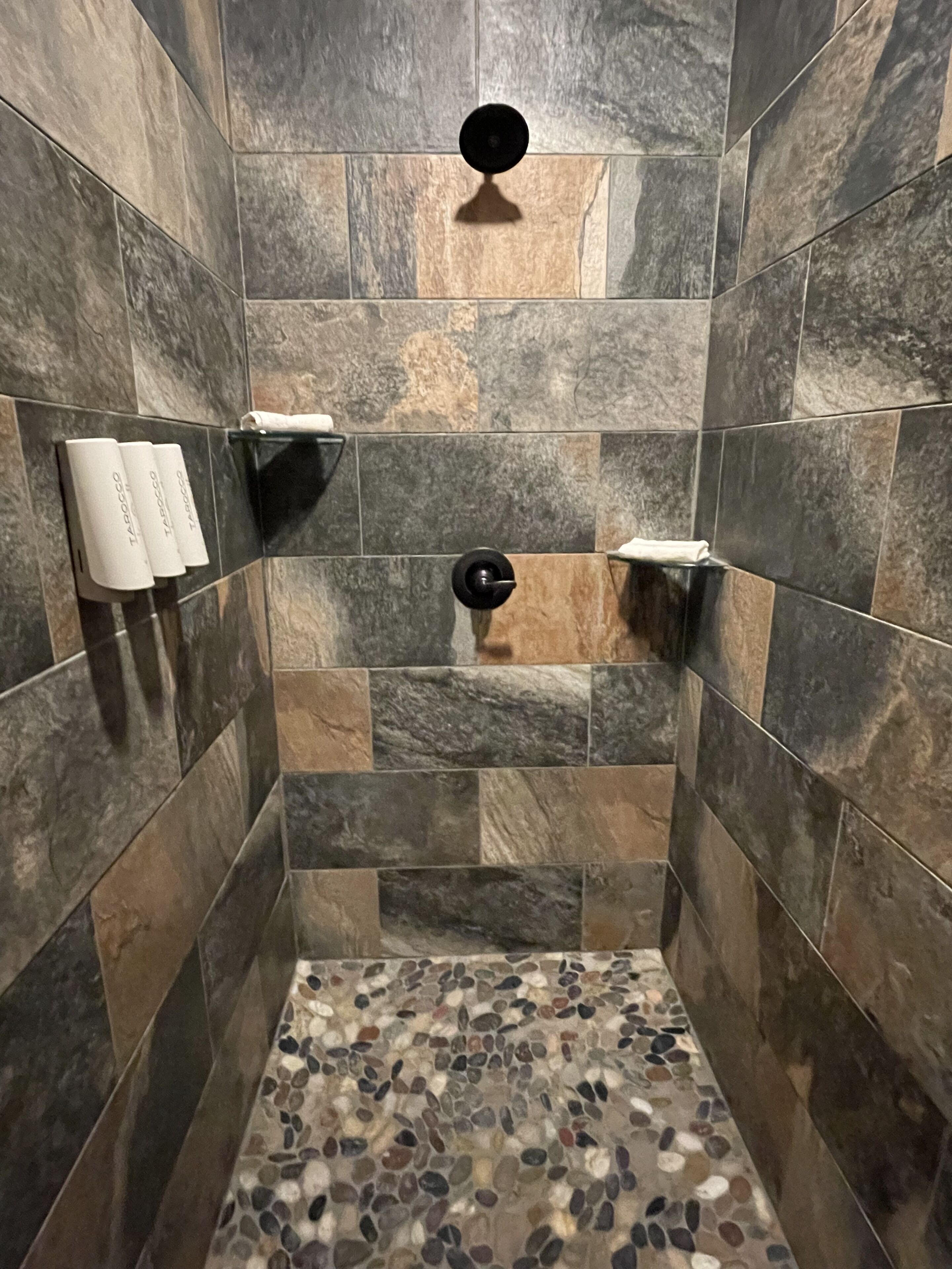 Un espace douche avec des carreaux de pierre et un sol décoré de motifs de galets.